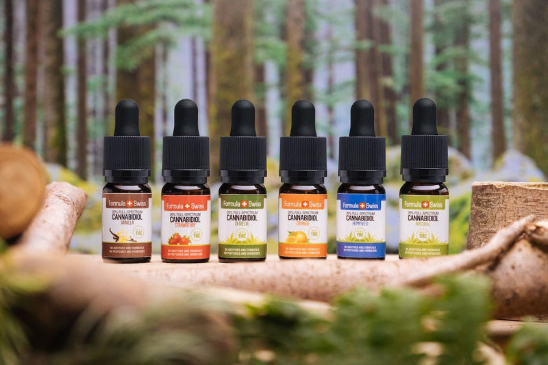 Six Formula Swiss full-spectrum CBD oils in different carrier oils and flavours, in front of a forest