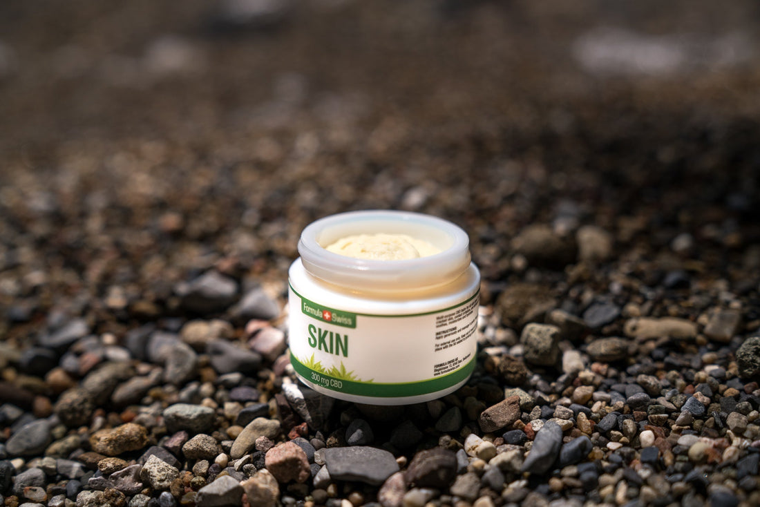 Open jar of Formula Swiss CBD Skin balm, 300 mg CBD, on a pebble beach